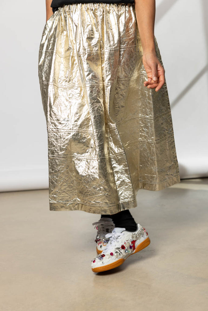 Person wearing a metallic gold skirt and bedazzled sneakers 